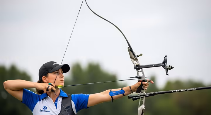 An Olympic archer at full draw, showing the complex setup of a recurve bow with stabilizers, a sight, and a clicker.
