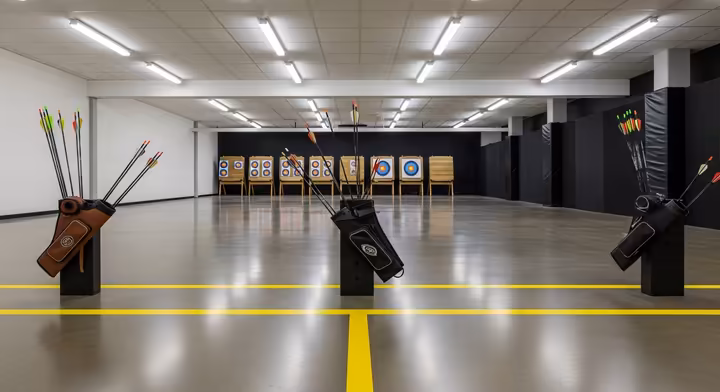 An indoor archery range showing a distinct shooting line and a waiting line a few feet behind it.